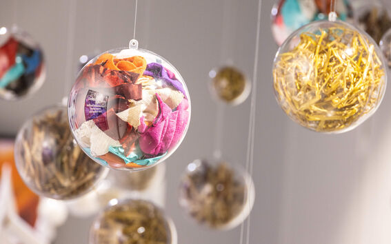 Hanging clear baubles filled with colourful fabric scraps and golden metal pieces against a soft background