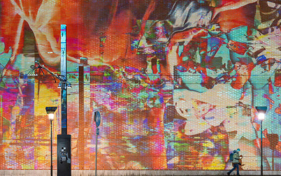 Henkilö kävelee värikkään tiiliseinällä olevan muraalin ohi, katuvalot ja sähkölaitteet yläpuolellaan.
