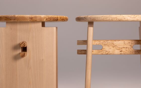 Two light wooden stools, one with a rectangular and one with a rounded structure, placed against a neutral background.