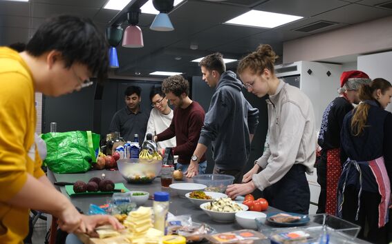 A group of people cooking together in a modern kitchen. Various vegetables and ingredients are on the counter.