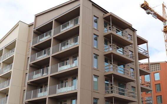 Modern wooden apartment buildings with multiple floors and balconies. A construction crane is visible in the background.