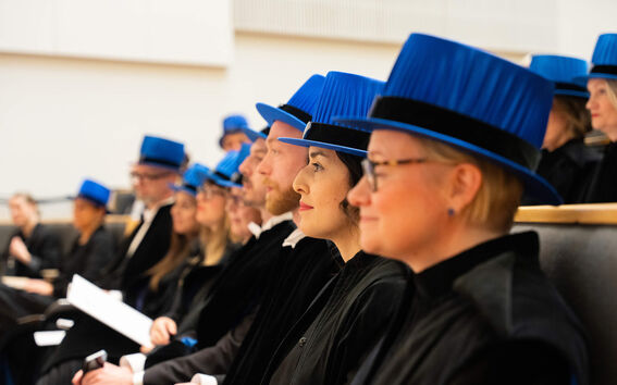 People wearing blue academic hats and black gowns seated in rows during a ceremony.