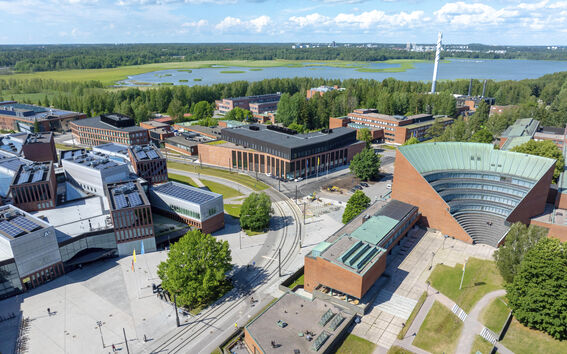 Ilmakuva Aalto-yliopiston kampuksesta Otaniemessä. Modernit rakennukset, viheralueet ja järvi taustalla.