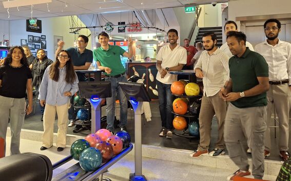 Several people stand in a bowling alley, some cheering and others watching. Bowling balls are visible in racks.