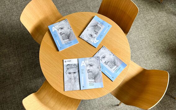 Viisi lehteä, joissa on harmaansininen kansi pyöreällä puupöydällä, jota ympäröi neljä puutuolia.