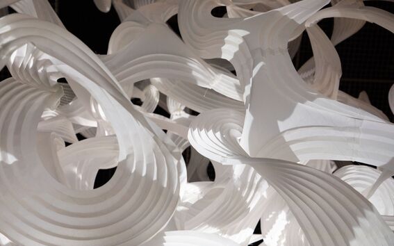 A complex, large installation of twisted white paper structures with various spirals and curves against a dark background.