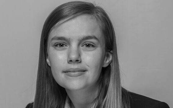 A person with shoulder-length hair wearing a striped shirt and a dark blazer.