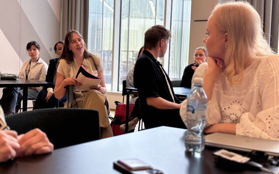 Joukko osallistujia istuu moderneissa tiloissa pöytien ympärillä; jotkut pitävät papereita ja keskustelevat. Kuva EDI-työpajasta kesäkuussa 2025.