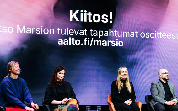 Four people sitting on chairs with a large screen behind them showing Aalto University's Marsio event information.