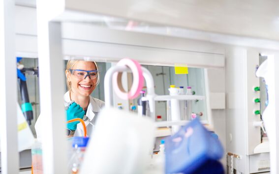 Tieteilijä, jolla on turkoosit käsineet, työskentelee laboratoriossa, joka on täynnä erilaisia ​​laitteita ja astioita.