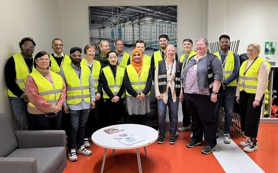 A group of people wearing yellow safety vests standing in an office with red flooring and a wall poster.