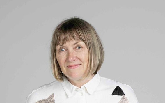 Henkilö pukeutuneena valkoiseen paitaan, jossa mustia ja beigejä abstrakteja kuvioita, lyhyet hihat, tummat housut.