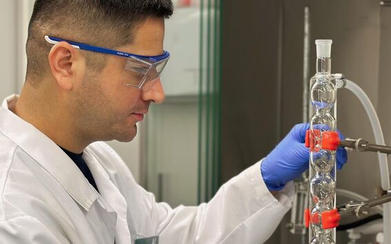 Person wearing blue gloves and a white lab coat working with glass laboratory equipment.