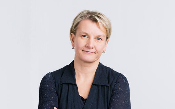 Woman with short blonde hair wearing a dark navy blue long sleeve shirt, arms crossed.