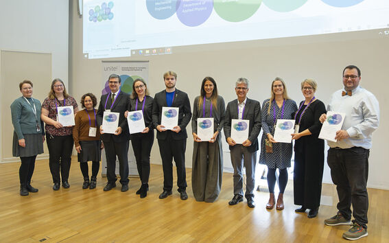 Group of people standing in a line holding certificates. A projector screen is visible behind them.