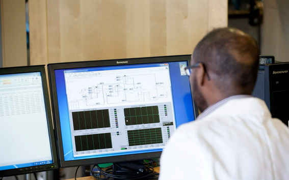 A person in a lab coat working at a desktop computer with multiple screens displaying data and charts.