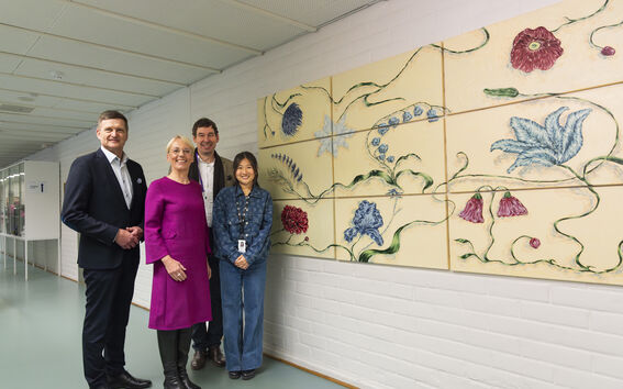 Four people stand in a hallway, looking at a large floral artwork mounted on the white brick wall.