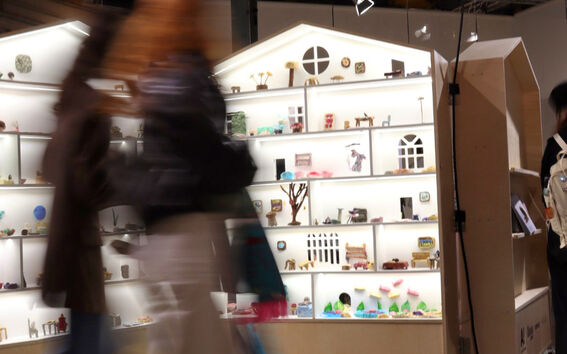 Valaistu talonmuotoinen näyttelykaluste, jonka edessä kävelee kaksi ihmistä