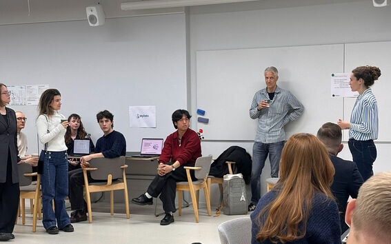 In a bright room, a group of people talking, some sitting, some standing.
