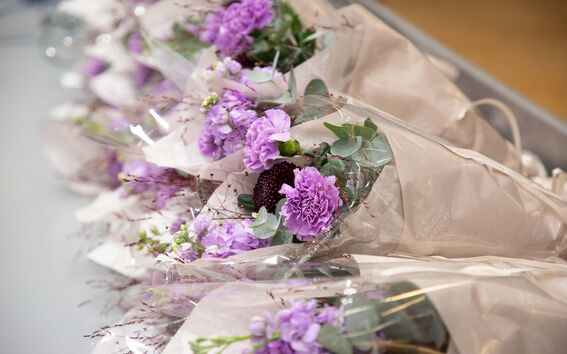 Useita violetteja kukkakimppuja ruskeassa paperissa rivissä pöydällä.