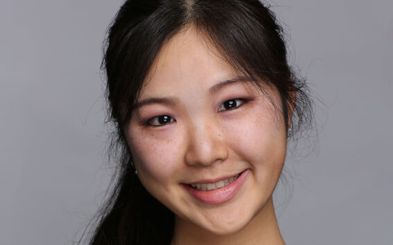 Henkilö, jolla on pitkät tummat hiukset, musta paita ja hopeinen kaulakoru, jossa on pyöreä riipus.