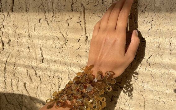 Käsi, jossa on läpinäkyvistä, meripihkanvärisistä rakenteista tehty rannekoru, lepää halkeilevaa seinää vasten.