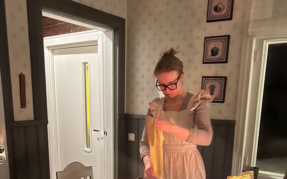 Henkilö valmistaa pastaa kodikkaassa keittiössä. Pöydällä on kynttilä, viinilasi ja jauhopussi.