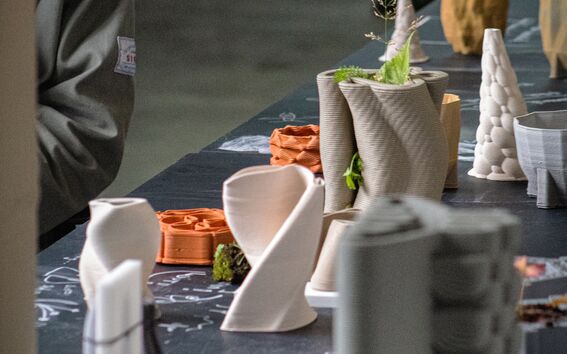 A table with various architectural models, including twisted and conical shapes, with a person partially visible on the left.