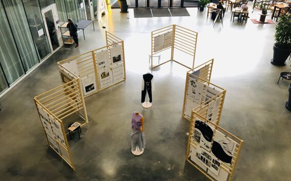 Exhibition space with mannequins and display boards. People are seated in the background near large windows.