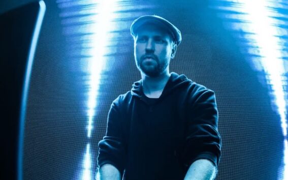 Person i mörk hoodie och keps använder DJ-utrustning med starka ljus i bakgrunden.