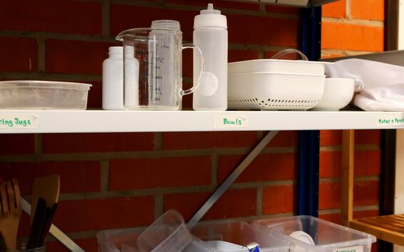 Shelves with various kitchen and laboratory items including measuring jugs, bowls, petri dishes, and utensils.