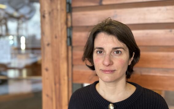 Person wearing a dark knitted cardigan with large buttons, standing in front of a wooden door.
