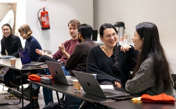 People sitting at tables with laptops and coffee cups, engaging in conversation.