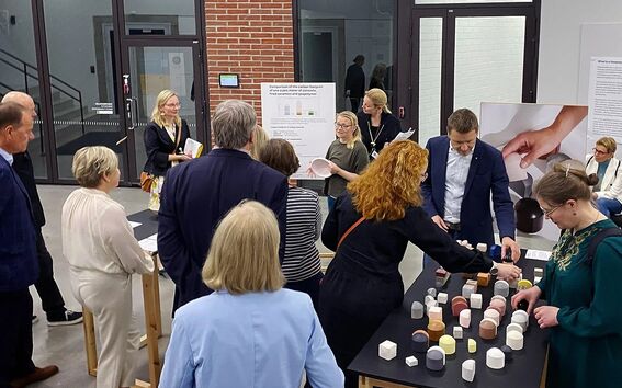A group of people are gathered around a table with various geometric objects. Posters are displayed on the walls.