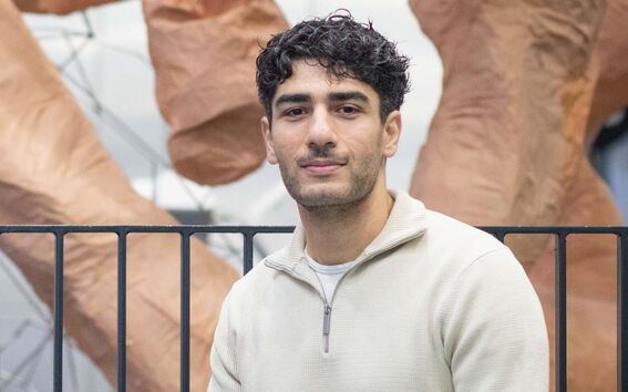 Henkilö, jolla on beige pusero ja siniset farkut, istuu veistoksen edessä, jossa on suuria ruskeita muotoja.