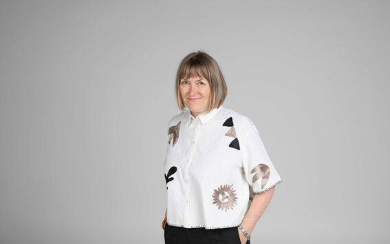 Person wearing a white shirt with abstract patterns and black trousers, standing against a grey background.