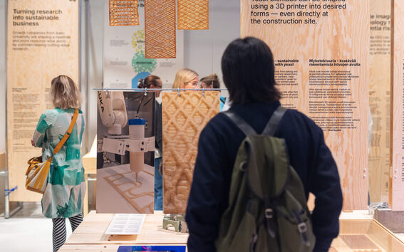 Ihmiset tarkastelevat puupintoja ja 3D-tulostettuja rakennusmateriaaleja näyttelyssä.