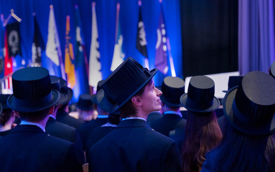 Valmistuneet tummissa puvuissa ja tohtorinhatuissa katsovat siniseksi valaistulle lippulavalle.