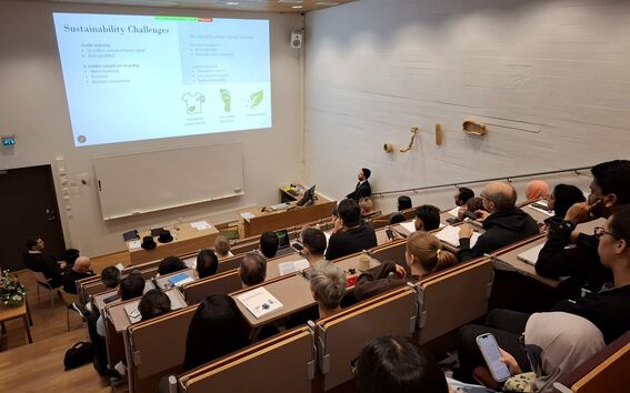 Students in a tiered lecture hall watch a sustainability slide projected on a white screen