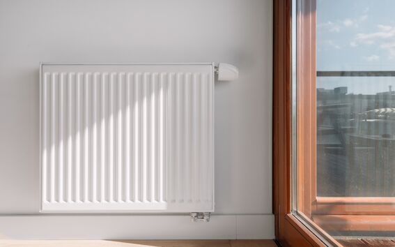 White panel radiator on a light wall beside a wooden-framed glass door with city view