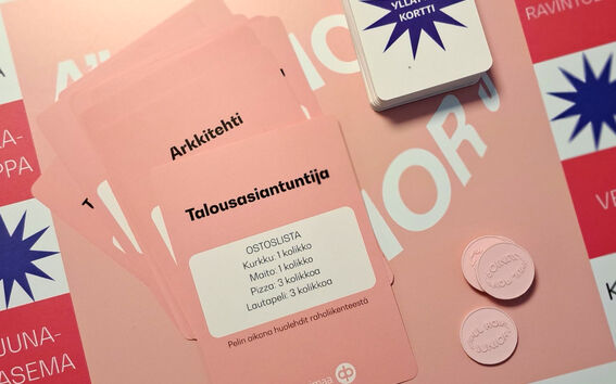 Lautapeli, jossa vaaleanpunaiset kortit nimellä 'Arkkitehti' ja 'Talousasiantuntija', kolikot, ja 'Yllätyskortti'.