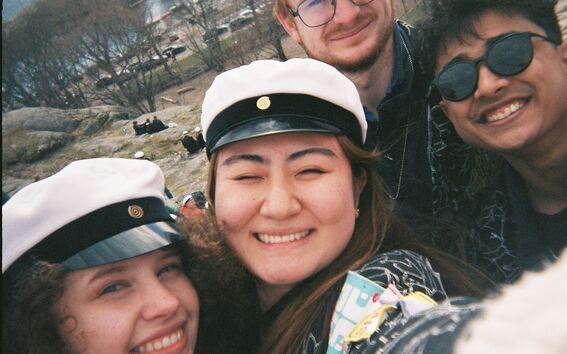 Group of people wearing white caps with black bands. The background shows a park with trees and a waterfront.