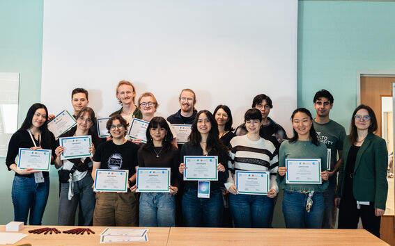A group of people holding certificates, standing indoors in front of a whiteboard.