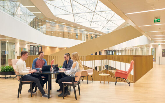 Business school main building. Students sitting around a table and working on their computers.