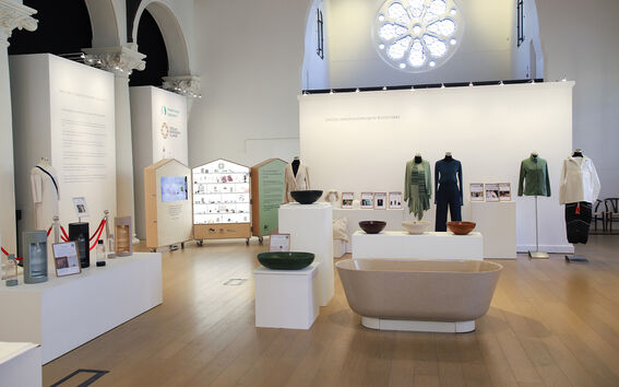 Moderni näyttelysali, mannekiineilla vihreitä ja valkoisia vaatteita, kulhoja ja beige kylpyamme jalustoilla