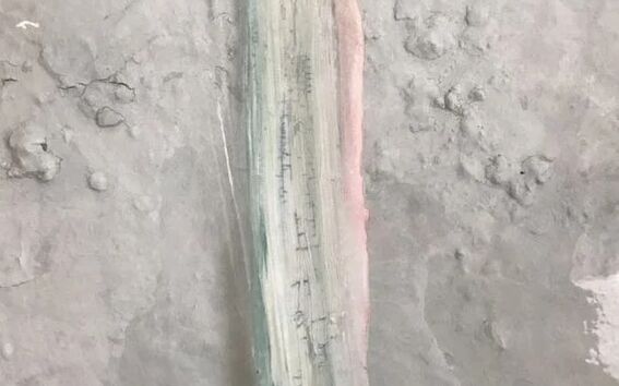 A rough surface with a vertical streak of green and pink paint in the centre, surrounded by greyish texture.