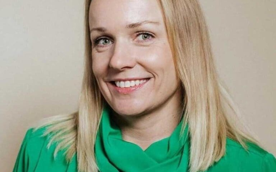 Henkilö, jolla on vaaleat puolipitkät hiukset ja kirkkaanvihreä pusero, kasvot sumennettu vaaleaa taustaa vasten