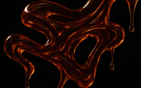 Abstrakti lähikuva kiiltävästä meripihkanruskeasta nesteestä, joka kiemurtelee ja tippuu mustalla taustalla