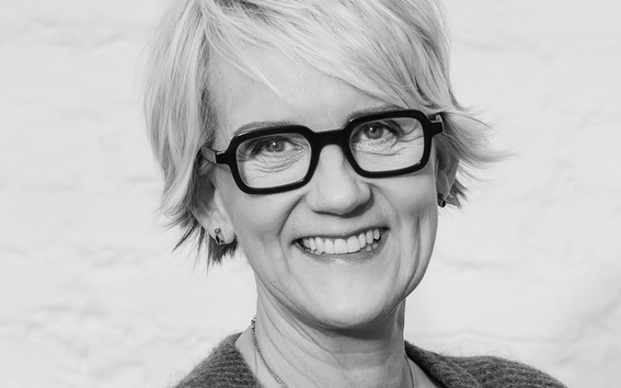 Mustavalkoinen muotokuva lyhyttukkaisesta aikuisesta neuleessa ja kaulakoruissa