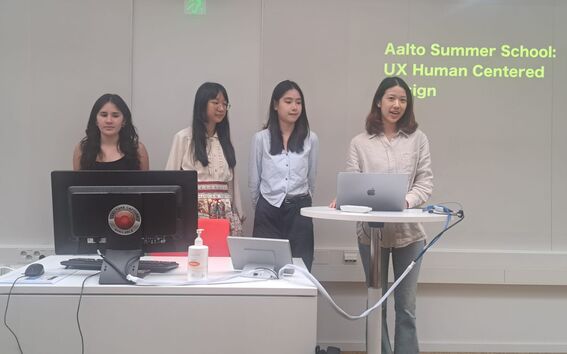 Four students stand by laptops presenting a UX project titled Aalto Summer School: UX Human Centered Design.